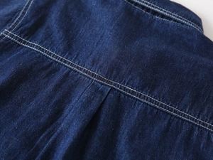 Detailed close-up of dark blue denim shirt yoke with precise white double stitching