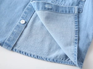 Close-up of light blue cotton denim shirt featuring white buttons and detailed stitching