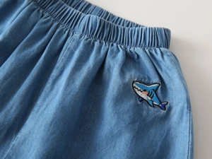Detail of light blue denim pants with elastic waist and cute shark embroidery for kids