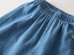 Detailed view of elastic waist and cute shark embroidery on light blue denim shorts