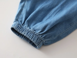 Detail of light blue denim pants featuring elastic ribbed cuffs and twill fabric texture
