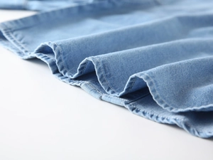 Macro detail of kids light blue denim shirt hem with premium double stitching