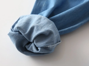 Detail shot of white overlock stitching on light blue denim fabric for kids pants