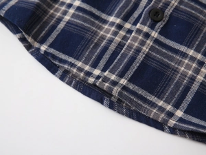 Macro detail of plaid shirt showing curved hem, fine stitching, and black resin button