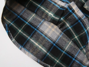 Détail d'une chemise en flanelle à carreaux bleu-vert montrant l'ourlet arrondi fini