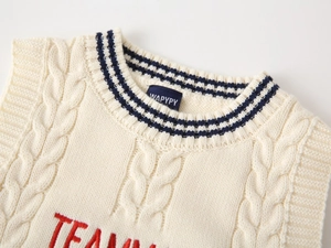 Detail of cable knit kids vest with embroidered letters and striped crew neckline