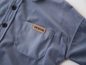 Detail of blue corduroy shirt featuring chest pocket and brown leather design label