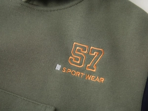 Detail of army green hoodie with embroidered orange number 57 and sport wear lettering