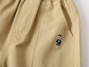 Close-up of khaki cotton trousers featuring detailed bear embroidery and elastic waistband