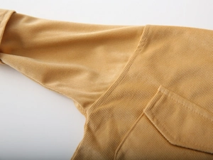 Detail of yellow corduroy fabric showing fine stitching and pocket texture on kids shirt