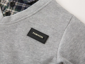 Detail of gray ribbed knit sweatshirt with green plaid shirt collar and fashion patch