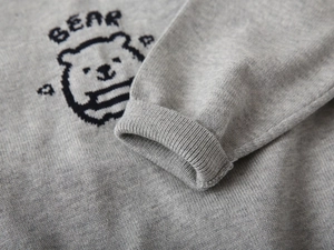 Close-up of gray knit sweater showing pixelated bear pattern and ribbed cuff detail
