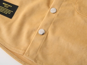 Macro shot of ginger yellow corduroy fabric with metal buttons and woven brand label