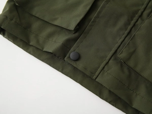 Detail of olive green kids jacket showing durable fabric pocket and snap button closure