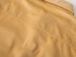 Detail of ginger yellow corduroy fabric showing fine stripes and neat double stitching