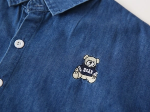 Detail of cute bear embroidery and white buttons on a boys denim long sleeve shirt