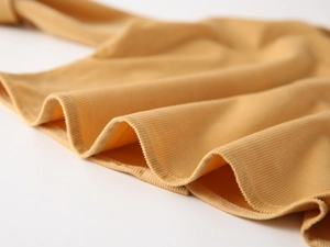 Detailed close-up of ginger yellow corduroy fabric with ruffled hem and precise stitching