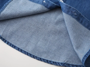Macro detail of boys denim shirt hem showing curved cut and neat stitching quality