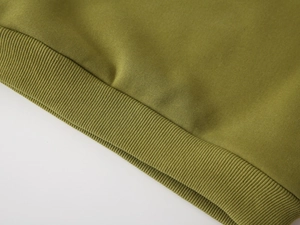 Detailed macro shot of the green ribbed knit hem and high-quality stitching on the sweatshirt