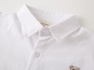 Close-up of boys' white cotton shirt featuring fine cartoon embroidery and button-down collar