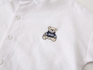 Detailed close-up of bear embroidery and white cotton fabric on boys long sleeve shirt