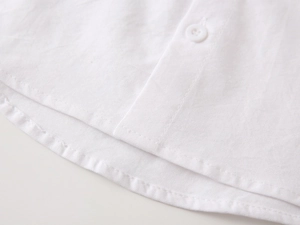 Macro detail of white cotton boy's shirt showing curved hem and premium stitching