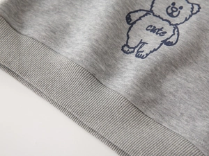 Detail of grey knitted sweater fabric with cute bear print and ribbed hemline