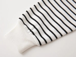 Detailed view of white ribbed cuffs and black striped knit fabric on kids' sweatshirt
