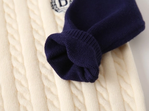 Detail of cable knit sweater featuring navy ribbed cuffs and embroidered letter B logo