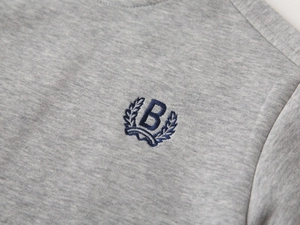 Gros plan du logo B brodé bleu sur le sweat-shirt en maille grise pour garçon