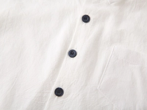 Close-up of white cotton shirt featuring black buttons and a square chest pocket detail