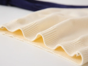 Detailed macro view of the cream knitted sweater's ribbed cuffs and soft fabric texture