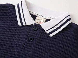 Detail of dark blue waffle knit boys' polo shirt showing white striped collar and texture