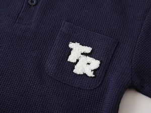 Detail of navy waffle knit polo shirt with a white TR letter towel embroidery patch