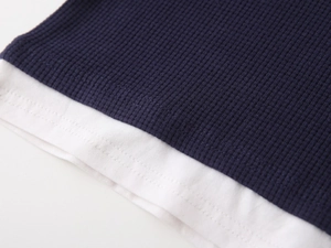 Close-up of boys' long sleeve polo with dark blue waffle knit and white layered hem detail