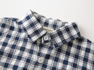 Gros plan du col de chemise à carreaux bleus pour garçon avec étiquette et boutons