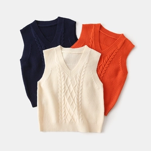 Detail of V-neck knitted vests in navy, cream, and orange with cable knit texture