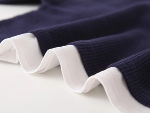 Close-up of kids' navy waffle knit fabric and layered white hem of a long sleeve polo
