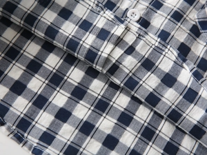 Détail d'une chemise à carreaux bleu et blanc montrant les coutures et un bouton