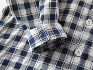 Détail macro du poignet de chemise à carreaux bleus avec bouton blanc et couture précise