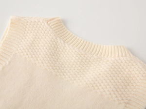 Close-up of off-white knit sweater showing ribbed V-neckline and textured shoulder weave