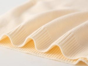 Close-up of the ribbed edge and soft knit texture on this cream white baby vest