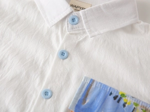 Close-up of boys' white cotton shirt with blue buttons and abstract print pocket detail