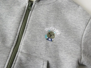 Détail du sweat à capuche gris pour enfant montrant le zip et la broderie animale