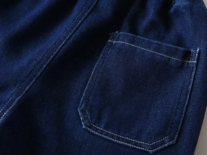 Macro detail of indigo denim jeans with white contrast stitching and elastic waistband