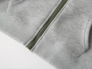 Détail de sweat à capuche gris pour enfant avec zip vert et texture en coton