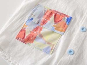 Detailed close-up of white cotton shirt with abstract painted pocket and blue buttons