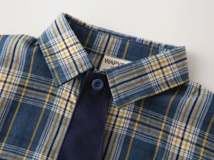 Gros plan du col de chemise à carreaux bleu enfant avec bouton et tissu en coton