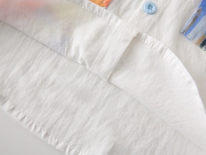 Close-up of white cotton baby shirt featuring colorful abstract prints and a blue button