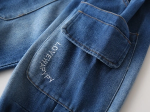 Detailed macro view of denim flap pocket with orange stitching and white embroidery